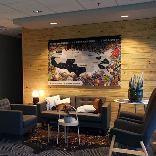 A cozy waiting area with dark gray armchairs and a small table featuring potted plants. A large, colorful map is mounted on a wooden wall, displaying data centers across the U.S. Soft lighting creates a warm atmosphere.