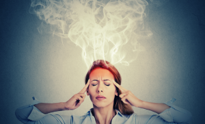 A woman with long hair closes her eyes and touches her temples. Her forehead is red, and white smoke billows upward, giving the impression of stress or a headache. The background is a plain grayish-blue.