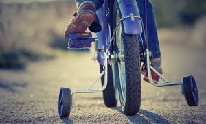 Child riding a bicycle with training wheels on a sunny day. Close-up of the rear wheel and the child's feet on the pedal, with a focus on the tire and training wheels.