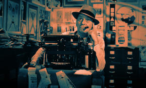 Man in a fedora sits at a desk with an old-fashioned typewriter in a cluttered room filled with posters and papers. He holds a pipe and gazes to the side thoughtfully. The sepia tone adds a vintage feel to the scene.