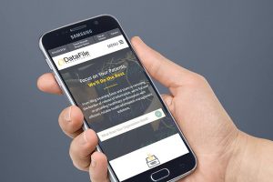 A hand holding a Samsung smartphone displaying a website. The screen shows the DataFile logo and a message: "Focus on your patients. We'll do the rest." There's a menu option at the top right corner and a query box at the bottom.