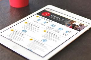 A tablet displaying a document titled "5 Components of Performance Review Process" with text and icons detailing points. The tablet rests on a dark surface with a red cup in the background.