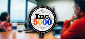 A meeting room with blurred figures seated at a table. The foreground features a circular badge with "America's Fastest-Growing Private Companies" around "Inc. 5000" in bold letters.