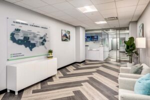 Modern office lobby with a white and gray herringbone floor. A wall map of the USA highlights data centers. White furniture and a potted plant decorate the space. Glass doors lead to other areas, and soft lighting brightens the room.