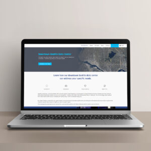 A laptop displaying a webpage for Downtown Seattle Data Center. The site features aerial images of Seattle and text about data center services, with a navigation menu at the top and contact details. The laptop is on a plain surface.