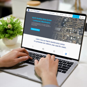 A person uses a laptop displaying a website for Digital Fortress, showcasing the North Seattle Data Center in Lynnwood, Washington. The website invites users to learn more or schedule a tour. The laptop is on a desk next to a small plant.