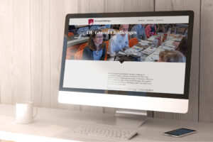 A computer monitor displays a website titled "D7 Grand Challenges" with a banner image showing people around a table. The page includes text and images of individuals collaborating in a bright, modern workspace.