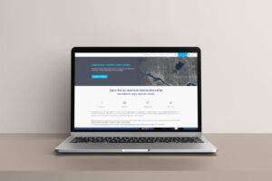 A laptop on a light-colored desk displays a website with a focus on a data center in downtown Seattle. The screen shows a map and text options such as Features, Floor Plans, and Contact. The overall design is clean and modern.