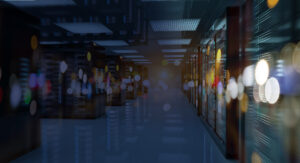 A dimly lit corridor in a data center is lined with server racks on both sides. Blurred bokeh lights create an abstract effect in the foreground, enhancing the futuristic atmosphere.