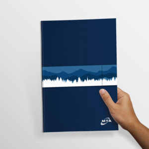 A hand holds a blue notebook with a design featuring white and dark blue silhouettes of trees and mountains. The notebook has a small white logo in the corner. The background is a plain white surface.