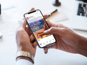 A person holding a smartphone displaying a travel-related app with a tropical image on the screen. The app features a promotion for sun, surf, and travel in the Atlantic. A notepad and pen are blurred in the background.