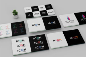 A display of various "ICON" logo designs on sheets of paper, featuring different fonts, colors, and styles. The sheets are arranged on a flat surface with a small potted cactus in the top left corner.