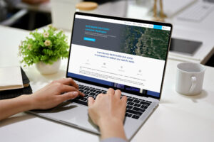 A person is using a laptop, displaying a website about the North Seattle Data Center in Lynnwood, Washington. The background features a plant and office supplies on a table.