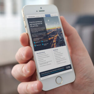 A hand holding an iPhone displaying a website about proactive monitoring and management for UCR and voice. The screen shows sections like 'Our UCR Services Include' with bullet points, and a cityscape image in the header.