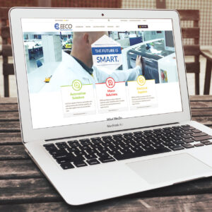 A MacBook Air on a wooden table displays a website for EECO. The webpage showcases services like Automation Solutions, Motor Solutions, and Electrical Supplies. A background image shows a person working in a technical environment.