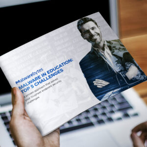 A person holds a brochure titled "Malwarebytes: Malware in Education, Top 5 Challenges," featuring a composite image of a smiling person and a bookshelf. It's aimed at addressing endpoint security in educational settings.