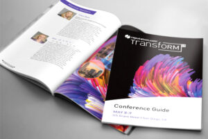 A conference guide titled "Transform 19" lies open on a table. The cover features vibrant, colorful brush strokes. The open page lists keynote speaker details and images. The event is on May 8-9 at the US Grant Hotel in San Diego, CA.