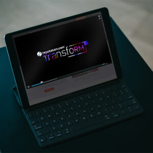 A tablet displaying a video with the title “reputation.com transform 19” on the screen. The device is placed on a folio keyboard on a dark surface. The background is dimly lit.