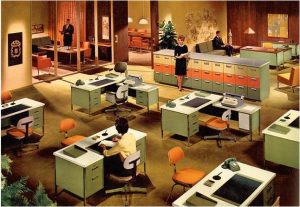 Retro office scene featuring several desks with green and orange chairs, typewriters, and rotary phones. People are standing and working around the room, with a mix of art and furnishings typical of mid-20th century design.